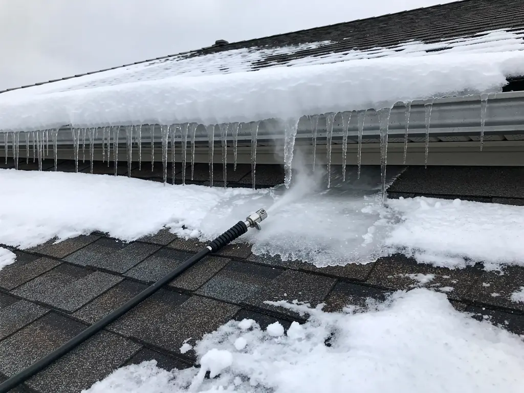 Snowy roof eave with an ice dam and icicles, steam rising where a channel has been melted through to the shingles